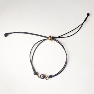 Detail of adjustable black woven bracelet with purple evil eye bead and gold slider