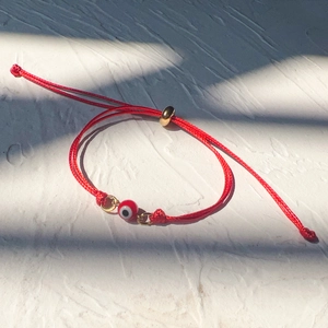 Close-up of red braided evil eye bracelet with gold adjustable slide clasp and bead
