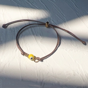 Detail of adjustable brown woven rope bracelet with yellow evil eye bead and gold sliding clasp