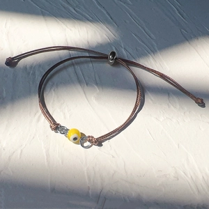 Detail of adjustable woven cord bracelet with a yellow evil eye bead and silver rings