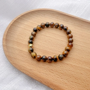 Macro shot of tiger eye beads bracelet with polished golden bead on a wooden tray