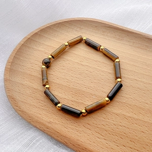 Detail of tiger eye stone beads and gold spacers on a wooden tray with soft lighting