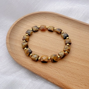 Macro shot of faceted square tiger eye stones with gold spacer beads on a wooden tray