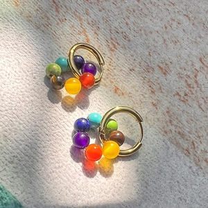 Boucles d'oreilles yoga en acier doré avec sept pierres de chakra sur surface en pierre