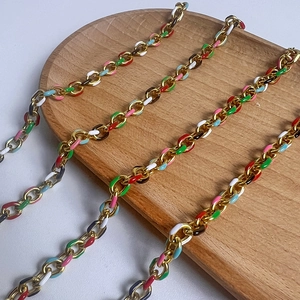 Macro shot of colorful enamel drips on gold metal O-chains over a wooden tray