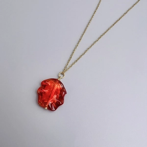 Detailed macro of a bohemian wrinkled red glass pendant with gold glitter on a gold chain
