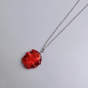 Detail of bohemian irregular red glass pendant with shimmering gold foil on silver chain