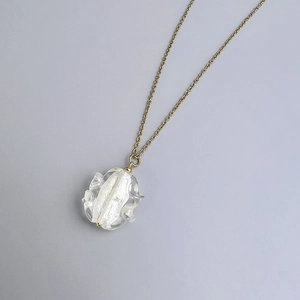 Macro shot of gold chain with irregular glass pendant and white textured interior detail