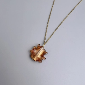 Macro detail of amber glass pendant with gold foil on a minimalist gold chain