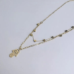 Detail of 18K gold layered necklace featuring Hamsa Hand pendant and heart charms