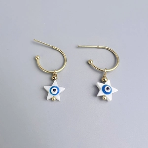 Detail of gold C-shaped earrings featuring white star charms with blue evil eye accents