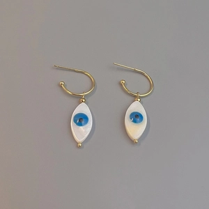Close-up of golden evil eye drop earrings with white shell inlay and blue accents