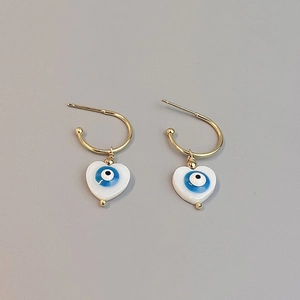 Close-up of golden heart earrings with blue evil eye enamel charms on grey background