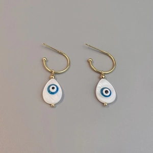 Macro shot of gold C-shaped earrings with white shell drop and blue evil eye detail