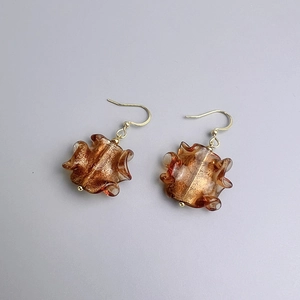 Détail de boucles d'oreilles en verre ambré avec feuilles d'or et design plissé vague