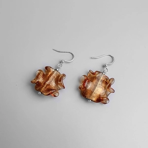 Gros plan de boucles d'oreilles en verre ambré avec plis ondulés et paillettes dorées