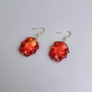 Détail macro de boucles d'oreilles pendantes rouges en résine avec crochets dorés et dorure