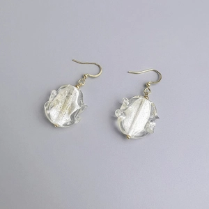 Détail de boucles d'oreilles crochet dorées avec breloques en verre et feuilles d'argent