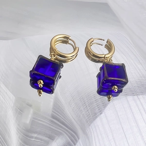 Détail de boucles d'oreilles en acier doré 18K avec pendentifs cubes en verre bleu