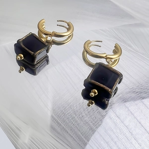 Détail de boucles d'oreilles en acier doré 18K avec pendentifs carrés en émail noir