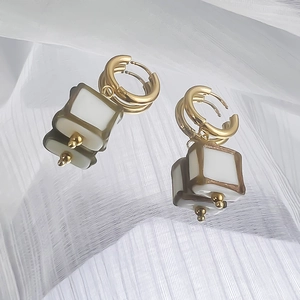 Détail de créoles dorées 18K avec pendentifs carrés en émail blanc sur tissu plissé