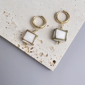 Détail de créoles dorées avec pendentifs carrés blancs sur plaque de pierre