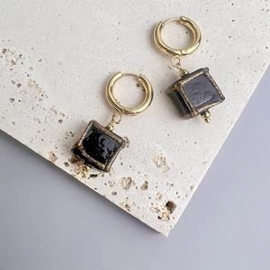 Détail de breloques en verre noir sur des boucles d'oreilles en acier doré 18 carats