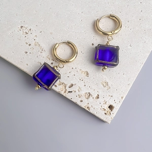 Détail de boucles d'oreilles pendantes en verre bleu et anneaux en acier plaqué or 18 carats