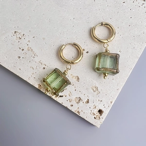 Détail de boucles d'oreilles en acier doré avec pendentifs en verre vert sur pierre