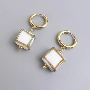 Gros plan détaillé de boucles d'oreilles en acier doré 18K avec pendentifs carrés blancs