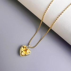 Nahaufnahme von Herz-Glasanhänger mit gelbem Blumenmuster an goldener Kugelkette