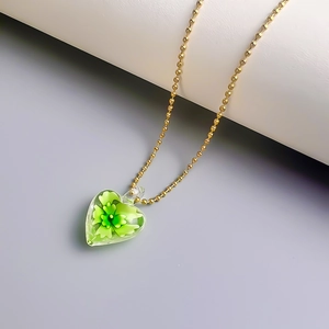 Nahaufnahme der goldenen Kugelkette mit einem herzförmigen Glasanhänger und grüner Blüte
