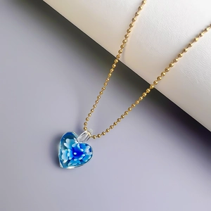 Detailaufnahme eines blauen Herzanhängers mit Blumen und goldener Kugelkette auf Dekors