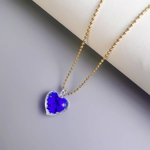 Detail einer goldfarbenen Perlenkette mit Kristall-Herzanhänger und blauen Blütenblättern