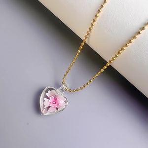 Detailaufnahme des herzförmigen Glasanhängers mit rosa Blume an goldener Kugelkette