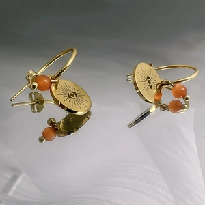 Détail de boucles d'oreilles œil de démon dorées avec perle d'opale orange sur fond poli
