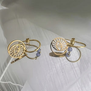 Détail de boucles d'oreilles en acier doré avec des pierres œil de chat bleu clair