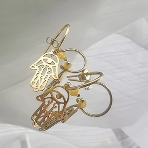 Vue macro de boucles d'oreilles Main de Fatma dorées avec perles d'ambre et détails ajourés