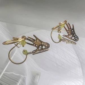 Détail de boucles d'oreilles dorées en forme de main avec motif d'œil et perles vertes