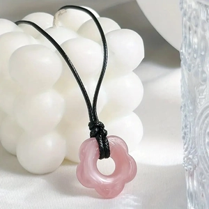 Close-up of pink flower resin pendant on black wax cord over white aesthetic background