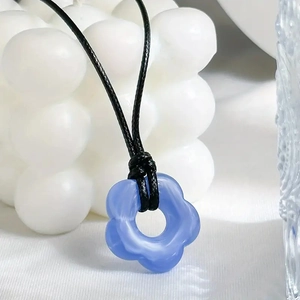 Close-up of a blue resin flower pendant on a black cord necklace with artistic background