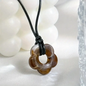Detailed close-up of hollow flower pendant with ink texture on black cord necklace
