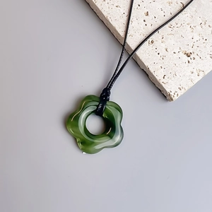 Detailed shot of a green floral pendant necklace with a black braided cord on stone
