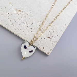 Detail showing the white glass heart pendant with black patterns on a gold paperclip chain