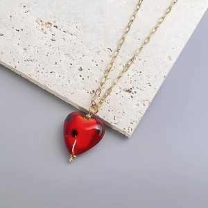 Detail of red heart glass pendant with hand-painted dots and golden chain on stone base