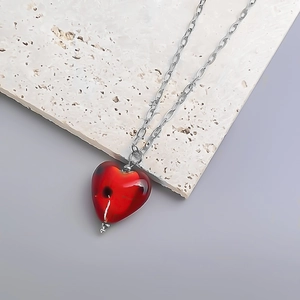 Macro shot of 3D red heart glass pendant with hand-painted dots on a silver metal chain