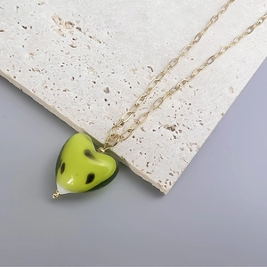 Macro view of green glass heart pendant with black patterns on a gold metal chain