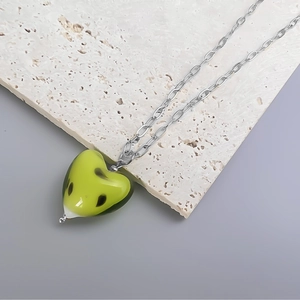 Detailed view of yellow hand-painted heart pendant on a silver-tone chain over stone