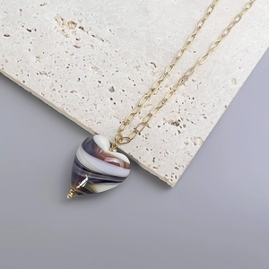 Close-up of heart-shaped glass pendant with colorful marble texture on a gold chain