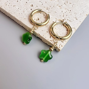 Gros plan de créoles dorées avec pendentifs fleurs en opale verte sur pierre blanche